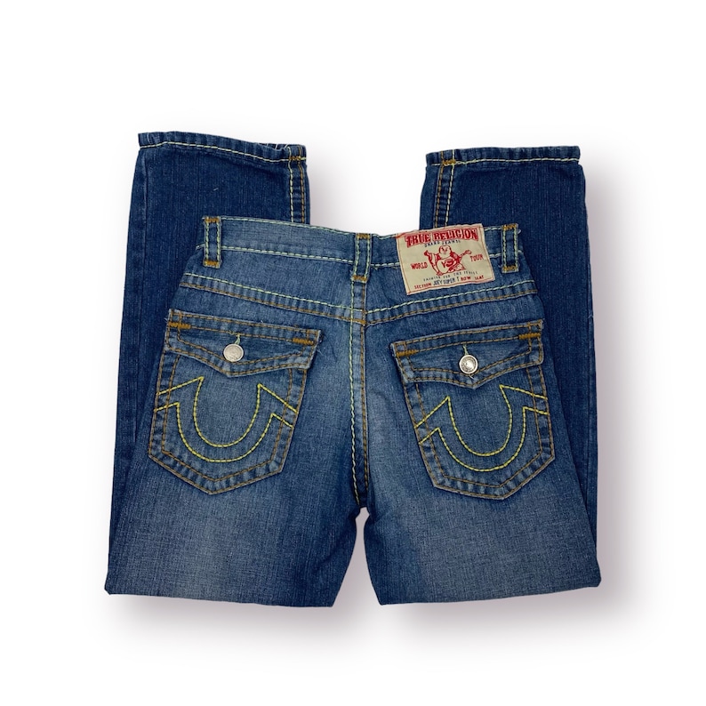 May include: A pair of blue denim jeans with yellow stitching and a True Religion patch on the back. The jeans have a horseshoe-shaped design on the back pockets.