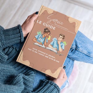 Może przedstawiać: Osoba trzyma książkę zatytułowaną "LE GUIDE". Okładka zawiera ilustracje dwóch studentów pielęgniarstwa oraz tekst "Survie d'un étudiant en soins infirmiers". Dodatkowy tekst brzmi "TESTÉ, APPROUVÉ ET SURVÉCU: TOUT CE QUE J'AURAIS AIMÉ QU'ON ME DISE".