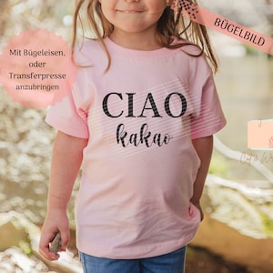 May include: A light pink t-shirt with the words "CIAO kakao" in black. The text is slightly angled with a striped design behind it. The shirt is on a young person.