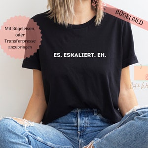 May include: Black t-shirt with the white text "ES. ESKALIERT. EH." printed across the chest. The shirt has short sleeves and a crew neck. The image also includes text in German: "Mit Bügeleisen, oder Transferpresse anzubringen."