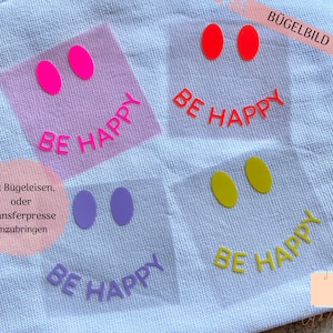 Könnte beinhalten: Vier Bügelbilder mit dem Text "BE HAPPY" in verschiedenen Farben. Die Bügelbilder befinden sich auf einem weißen Stoffuntergrund. Die Bügelbilder sind für die Verwendung mit einem Bügeleisen oder einer Heißpresse.