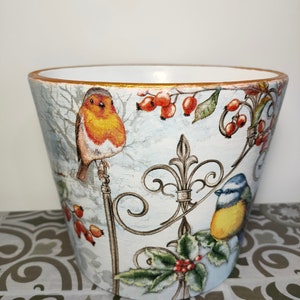 May include: A white ceramic planter with a blue and gold rim. The planter features a wintery scene with birds, berries, and holly.