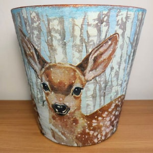May include: A ceramic planter featuring a painted image of a fawn in a snowy woodland setting. The planter is decorated with shades of blue, brown, and white.