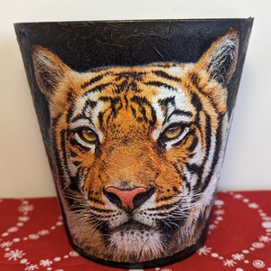 May include: A black planter featuring a close-up image of a tiger's face. The tiger has orange and black stripes and a white muzzle.