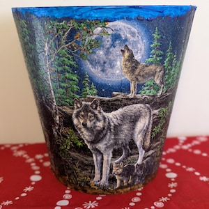 May include: A blue ceramic planter featuring a wolf howling at the moon design. The planter depicts a full moon, trees, and three wolves in a woodland scene.