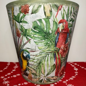 May include: A green ceramic planter with a tropical print featuring parrots, palm leaves and flowers. The planter has a distressed, textured finish.