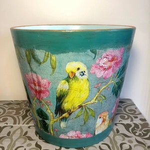 May include: Teal planter with a distressed finish featuring a floral design with pink flowers and yellow and blue birds.