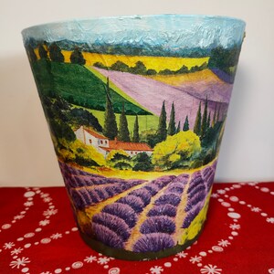 May include: A painted ceramic planter featuring a scene of a lavender field with a small house in the distance. The planter is painted in shades of green, yellow, purple, and blue.