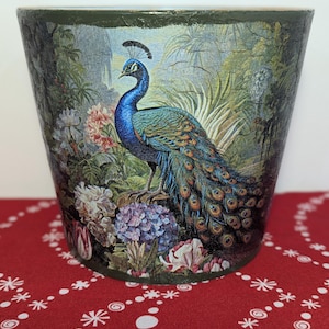 May include: A green ceramic planter featuring a peacock and floral design. The peacock is blue and green with a long tail. The flowers are pink, white, and purple.