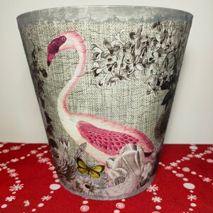 May include: A grey planter with a floral design featuring a pink flamingo and a butterfly. The planter has a textured surface and a silver rim.