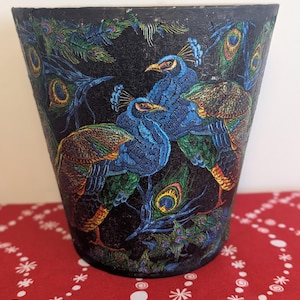 May include: A black decorative vase with a detailed peacock design. The vase features vibrant blue, green, and orange peacock illustrations. The design includes peacock feathers and the birds themselves, creating a colorful and artistic piece.