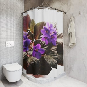 Puede incluir: Una cortina de ducha blanca con un estampado floral morado y verde. Las flores son violetas africanas con hojas verde oscuro.