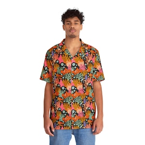 May include: Short-sleeved shirt with a colourful coral reef pattern. The design features orange, pink, green, and blue elements on a black background. The shirt has a classic collar and is worn with blue jeans.
