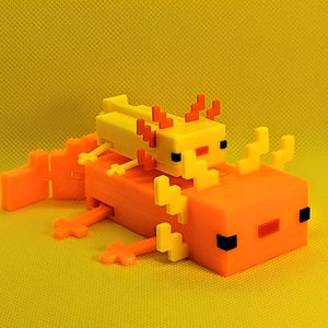 May include: A 3D-printed orange and yellow axolotl toy. The larger axolotl is orange with black and red accents, and the smaller one is yellow. The toy is designed with a pixelated aesthetic, reminiscent of a video game.