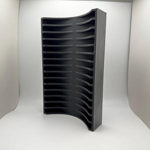May include: A black, vertical organizer with multiple curved shelves. The organizer is made of a solid material and has a curved front. The shelves are evenly spaced and appear to be designed for storing items. The product is set against a white background.