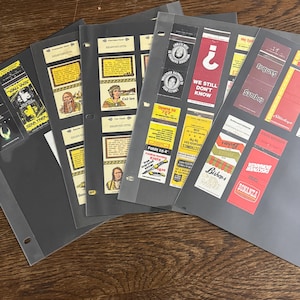 May include: A collection of vintage advertising cards and labels, displayed in clear plastic sleeves. The cards feature various designs, including text and illustrations. Some cards have text like "STAR TREK", "Col-lee", and "BONANZA".
