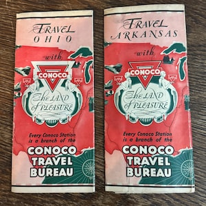 May include: Two vintage travel brochures, one for Ohio and one for Arkansas, with a red and pink color scheme. The brochures feature the Conoco logo and the phrase "The Land of Pleasure."