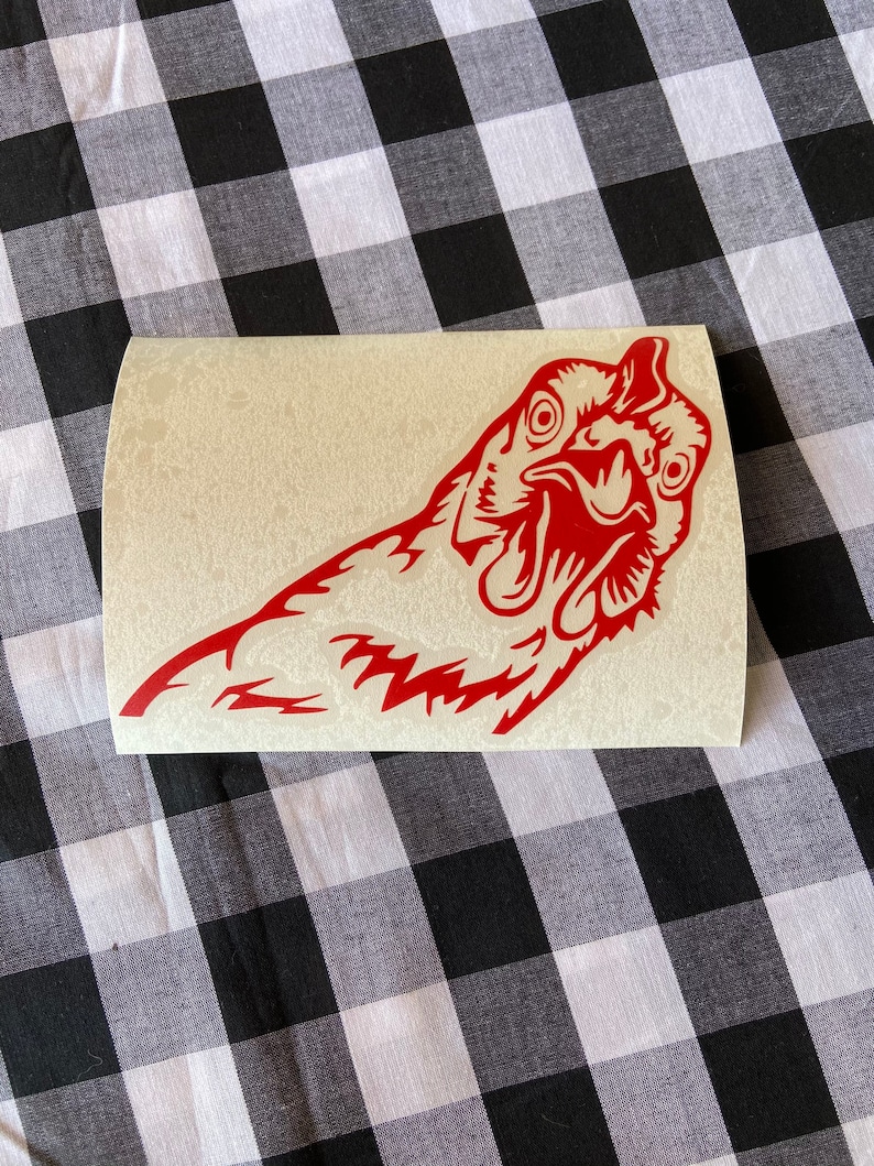 May include: Red vinyl sticker of a chicken's head with its beak open, looking directly at the viewer.