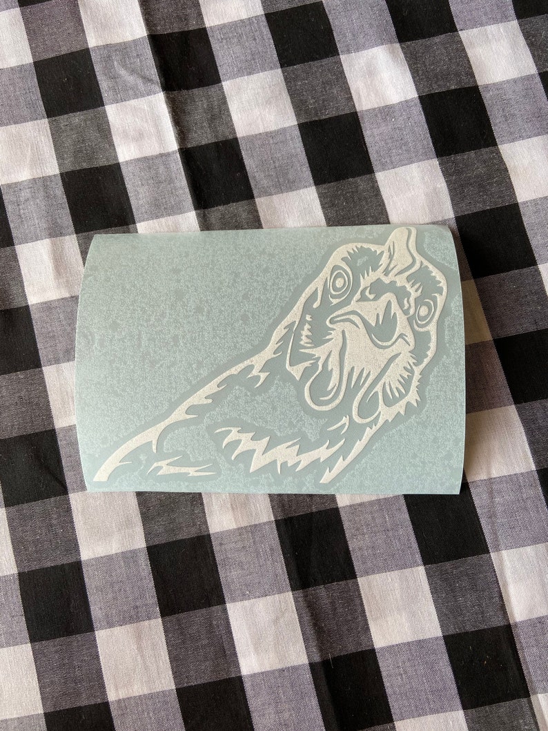 May include: White vinyl sticker of a rooster's head with an open beak and a detailed design. The sticker is on a light blue background.