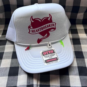 Puede incluir: Una taza de cerámica blanca con asa negra y el texto "But First, Coffee" en negrita negra. La taza se encuentra sobre un fondo borroso, sugiriendo un ambiente acogedor.