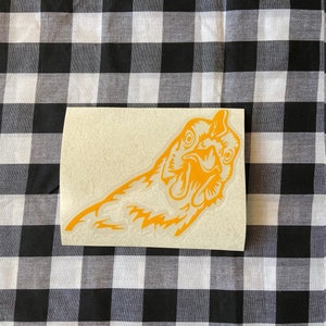 May include: A yellow vinyl sticker of a chicken's head with its beak open. The sticker is on a white background.