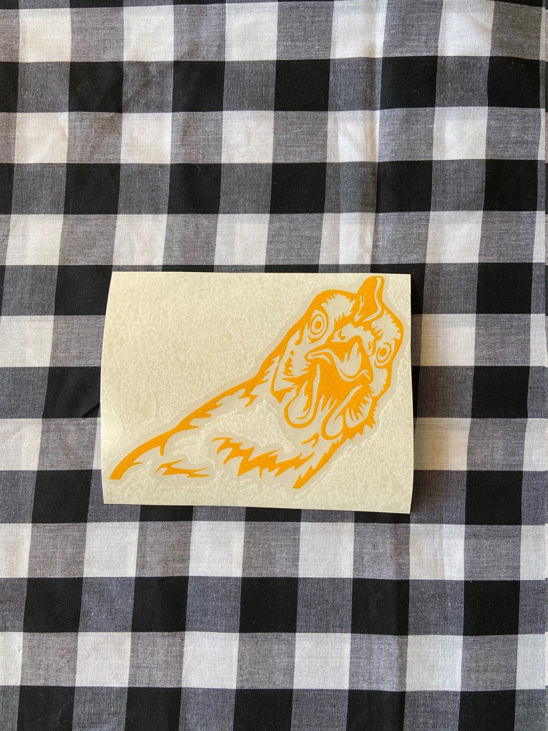 May include: A yellow vinyl sticker of a chicken's head with its beak open. The sticker is on a white background.