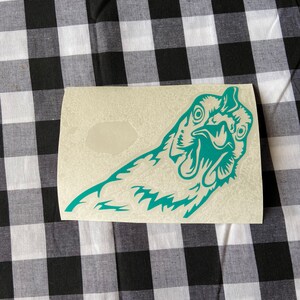 May include: A teal blue vinyl sticker of a chicken's head with its beak open. The sticker is on a white background.