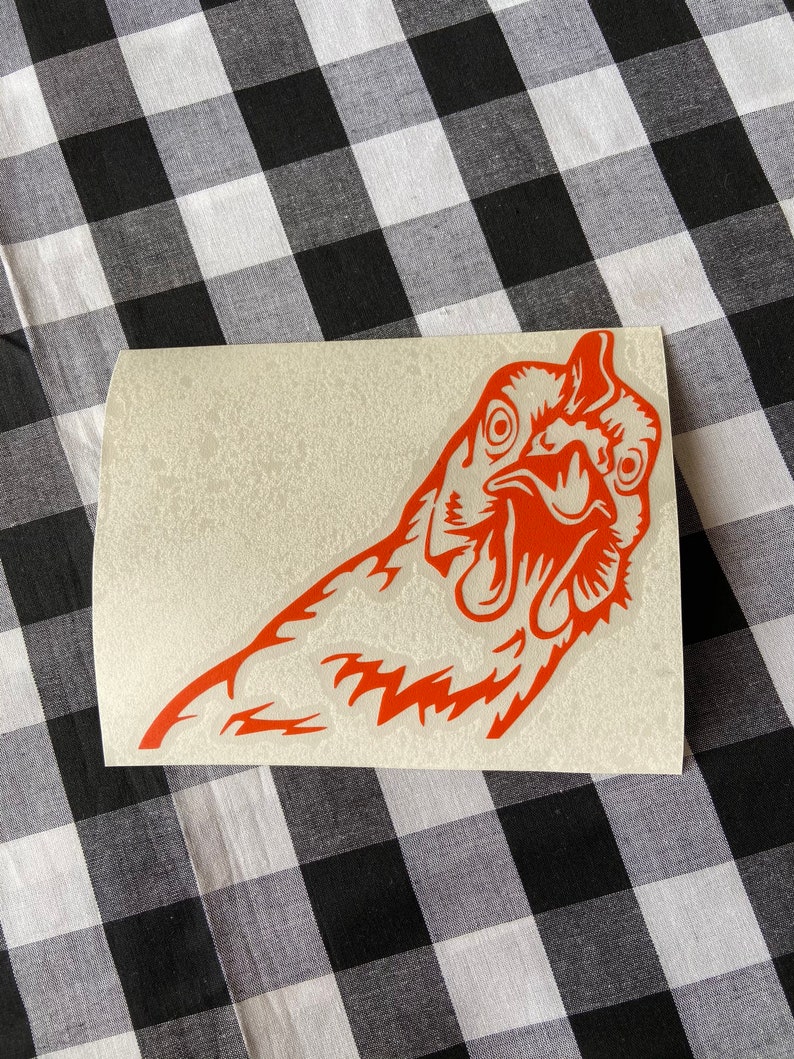 May include: A red vinyl sticker of a chicken's head with a surprised expression. The sticker is on a white background.