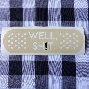 May include: A beige band-aid with white polka dots and the text "WELL, SH!T" in black lettering.