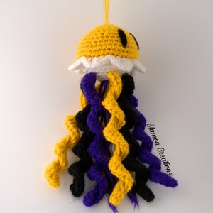 May include: A crocheted jellyfish toy with a yellow body, white frilly edges, and black eyes. The tentacles are crocheted in yellow, purple, and black.