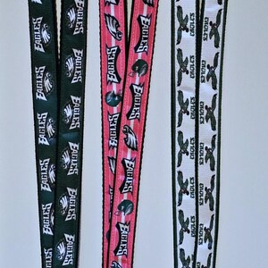 Puede incluir: Tres llaveros diferentes con cord&oacute;n y el logotipo de los Philadelphia Eagles. El primer cord&oacute;n es verde con letras blancas, el segundo es rosa con letras blancas y el tercero es blanco con letras verdes. Cada cord&oacute;n tiene un llavero plateado.