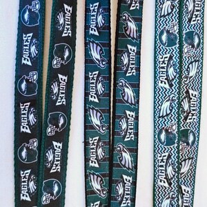 Puede incluir: Cuatro cordones de cinta verde y negro con el logotipo de los Philadelphia Eagles y el nombre del equipo repetido. Los cordones tienen diferentes patrones, incluyendo rayas, zigzags y un fondo verde s&oacute;lido.