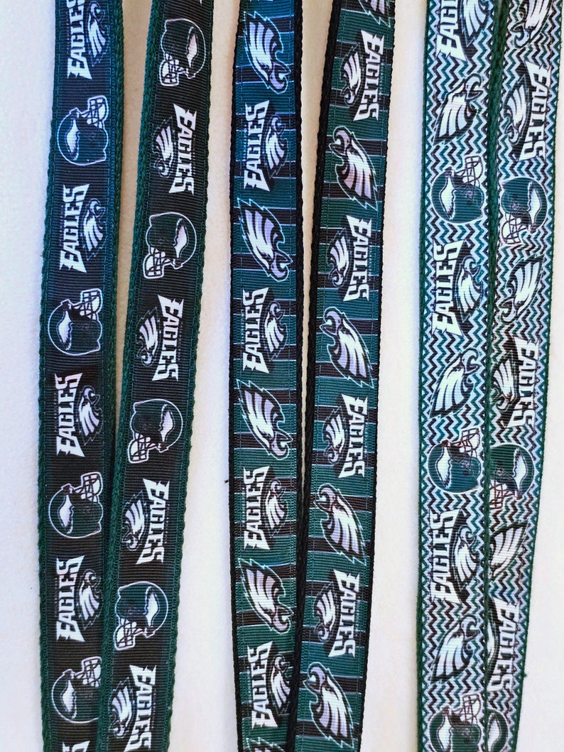 Puede incluir: Cuatro cordones de cinta verde y negro con el logotipo de los Philadelphia Eagles y el nombre del equipo repetido. Los cordones tienen diferentes patrones, incluyendo rayas, zigzags y un fondo verde s&oacute;lido.
