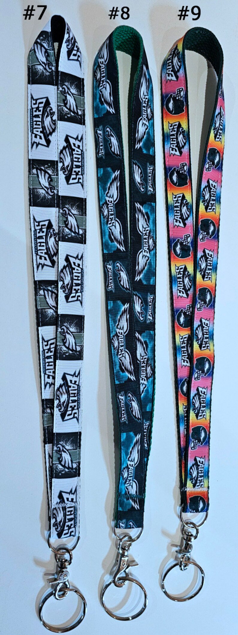 Puede incluir: Tres llaveros con cord&oacute;n diferentes de los Philadelphia Eagles. El primer llavero tiene un dise&ntilde;o en blanco y negro con el logotipo de los Eagles y la palabra "Eagles" repetida. El segundo llavero tiene un dise&ntilde;o en azul y negro con el logotipo de los Eagles y la palabra "Eagles" repetida. El tercer llavero tiene un dise&ntilde;o de arco&iacute;ris con el logotipo de los Eagles y la palabra "Eagles" repetida.