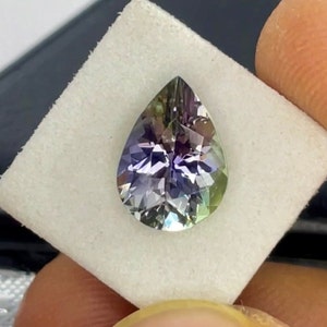 May include: A pear-shaped gemstone with a green, purple and blue colour gradient. The gemstone is faceted and has a high degree of brilliance.