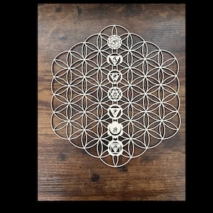 May include: A white wooden mandala with a flower of life design and seven chakras symbols in the center. The chakras are represented by different colors and symbols.