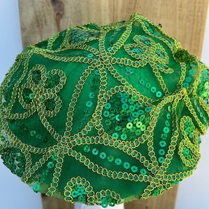 Op de afbeelding: Een groene baret met gouden pailletten en borduurwerk. De baret is versierd met een draaiend patroon.