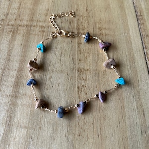 May include: A gold chain bracelet with small, irregular shaped stones in shades of blue, pink, and brown.