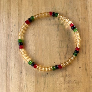 May include: A beaded bracelet with a pattern of red, green, and black beads on a clear background.