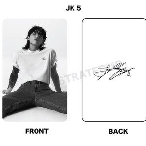 May include: Black and white photo of a person wearing a white t-shirt with a small logo and blue jeans. The person is sitting with their legs spread out. The back of the card has a black and white signature.