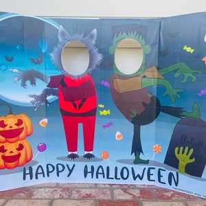 Puede incluir: Un telón de fondo de cabina de fotos de Halloween con dos recortes para caras. Un recorte es un hombre lobo con ropa roja y negra y el otro es Frankenstein con ropa marrón. El telón de fondo es azul con luna llena, murciélagos, caramelos y el texto "Happy Halloween".