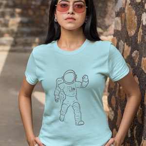 May include: A light blue t-shirt with a black and white illustration of an astronaut. The astronaut is wearing a helmet and is in a walking pose.
