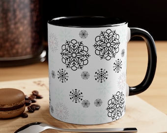 May include: A white ceramic mug with a black rim and handle. The mug features a repeating pattern of black snowflakes on a white background.