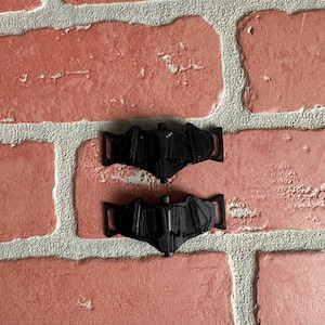 May include: Two black plastic shoe charms shaped like a bat. The charms are designed to be attached to shoelaces.