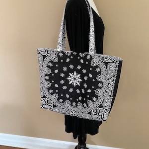 May include: Black and white bandana print tote bag with long handles. The bag is on a mannequin.