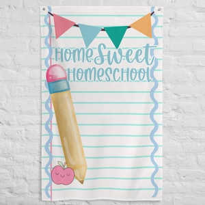 May include: White fabric wall hanging with the text "Home Sweet Homeschool" in light blue script. The design includes a large pencil, a pink apple, and a banner of colorful pennants. The background has horizontal blue lines.