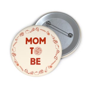May include: A round, off-white button with the text "MOM TO BE" in red. A red pizza graphic is in the center, surrounded by a red border of pizza-themed illustrations. A second button is visible in the background.
