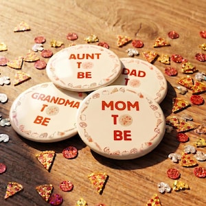 May include: Four round white buttons with orange text and pizza-themed illustrations. The buttons feature the phrases AUNT TO BE, DAD TO BE, GRANDMA TO BE, and MOM TO BE, each decorated with small pizza slice icons and various food-related graphics.