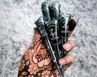 May include: Five black plastic cones filled with Jagua Henna paste, each featuring a circular label with the text "ZH Jagua Henna" and a small yellow tip. The cones are arranged in a cluster, showcasing a dark, intricate floral henna design.