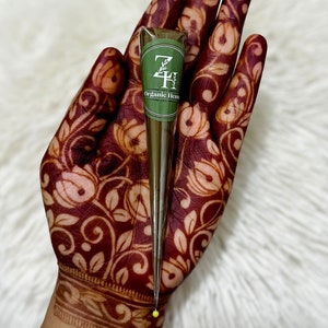 May include: A brown henna cone with a green label that says "ZH Organic Henna" on it. The cone is being held in a hand with a henna tattoo.